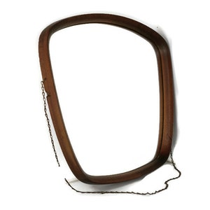 Puede incluir: Un espejo con marco de madera marrón con forma curva y una cadena para colgar.