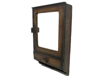 May include: A vintage wooden medicine cabinet with a rectangular mirror and a small drawer. The cabinet is stained a dark brown color and has a simple, rustic design. The door has a latch closure.