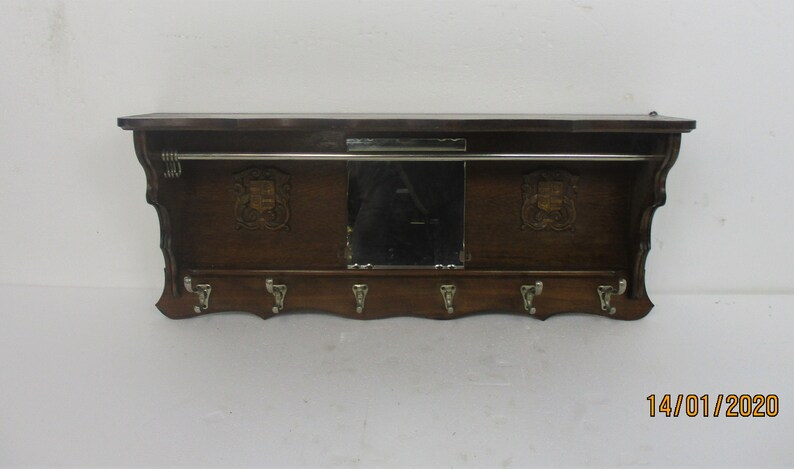 May include: A dark wood wall-mounted coat rack with a shelf, mirror, and coat hooks. The rack has a metal bar for hanging clothes and decorative crests either side of the mirror. The date 14/01/2020 is visible in the bottom right corner.
