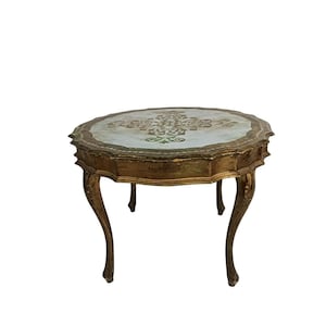 Könnte beinhalten: Ein antiker, achteckiger Beistelltisch mit einem goldfarbenen Holzrahmen. Die Tischplatte hat einen hellblauen Hintergrund mit einem gold-grünen Blumendesign. Der Tisch hat geschwungene Beine und einen gewellten Rand.