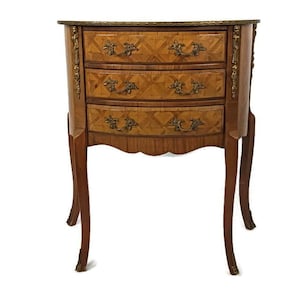 May include: A three-drawer wooden nightstand with a curved front and ornate brass hardware. The drawers are inlaid with a geometric pattern of wood veneers.