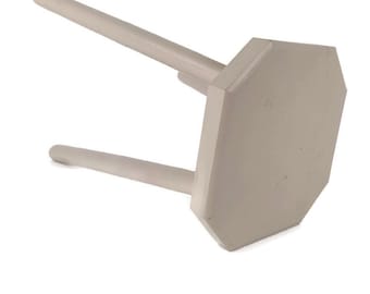 Könnte beinhalten: Ein hellbeige Holzstuhl mit achteckigem Sitz und drei zylindrischen Beinen. Der Hocker ist in einer neutralen Farbe lackiert und vor einem weißen Hintergrund platziert.