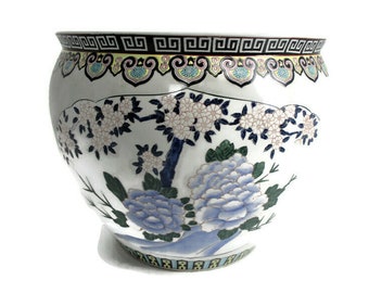 Könnte beinhalten: Ein großer weißer Keramiktopf mit einem blauen und weißen Blumendesign. Der Topf hat eine breite Öffnung und einen abgerundeten Körper. Das Blumendesign zeigt blaue und weiße Blumen, grüne Blätter und einen blauen und weißen Baum.