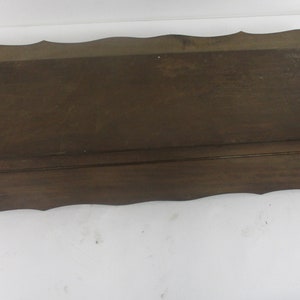 May include: A dark brown wooden shelf with a scalloped edge. The rectangular shelf is likely vintage and made of solid wood. The design is simple and classic, suitable for display or storage. The shelf's dimensions are not visible.