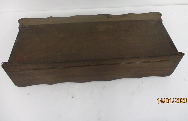 May include: A dark brown wooden shelf with a scalloped edge. The rectangular shelf is likely vintage and made of solid wood. The design is simple and classic, suitable for display or storage. The shelf's dimensions are not visible.
