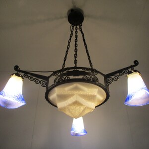 May include: An ornate, Art Nouveau-style chandelier with a black metal frame. It features three bell-shaped glass shades with blue speckles and a central geometric shade. The fixture hangs from a chain.