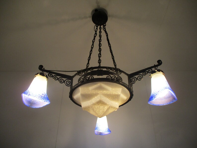 May include: An ornate, Art Nouveau-style chandelier with a black metal frame. It features three bell-shaped glass shades with blue speckles and a central geometric shade. The fixture hangs from a chain.