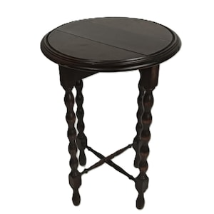 May include: A dark brown, round side table with a decorative edge. The table has four turned legs with a cross-shaped support near the bottom. The table is approximately 28 inches tall.