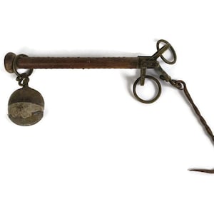 May include: A vintage, wooden-handled hanging scale with a metal hook and a round weight. The scale is made of brass and has a worn, antique finish.