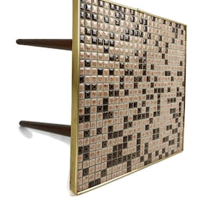May include: A square end table with a black and white mosaic tile top framed in brass. The table has two wooden legs.