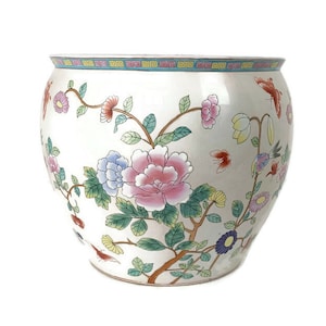 May include: A white ceramic planter with a floral design. The planter features pink, blue, and yellow flowers, green leaves, and red and blue birds. The planter has a blue and yellow border around the top.