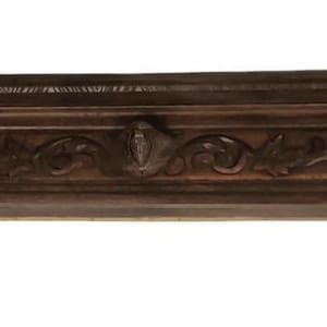 Puede incluir: Una repisa de madera marrón oscuro con detalles tallados de flores y volutas. La repisa tiene forma rectangular con un borde decorativo y es adecuada para una chimenea o una exhibición decorativa. La madera tiene un tono rico y cálido.