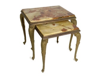 May include: A set of two nesting tables with ornate brass legs and a marble top. The top table has a light brown and green marble top, while the bottom table has a light green marble top.