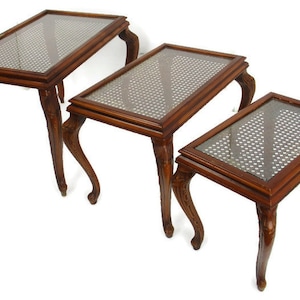 Könnte beinhalten: Ein Satz aus drei verschachtelten Tischen mit Glasplatten und aufwendig geschnitzten Holzbeinen. Die Tische sind aus dunklem Holz gefertigt und haben ein traditionelles Design.