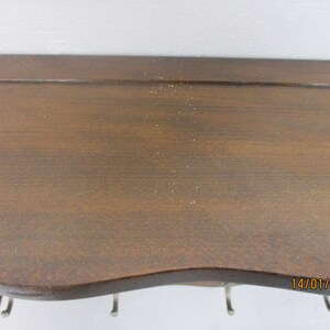 May include: A dark brown wooden shelf with a curved lower edge and several metal hooks. The shelf has a smooth surface and is mounted against a white wall. The shelf is designed for hanging items.