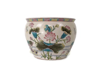 May include: A white ceramic planter with a floral design. The planter features blue, pink, green, and yellow flowers and leaves. The planter has a wide, round base and a narrow opening.