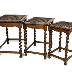 May include: A set of three antique wooden nesting tables. Each table features a square top with a woven design and ornate, turned legs. The tables are graduated in size, with the largest measuring approximately 61 cm wide.