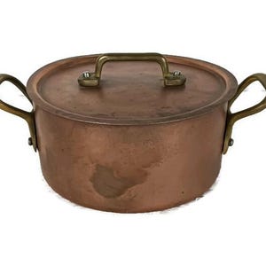 May include: A copper pot with brass handles and a lid. The pot has a worn, aged look.