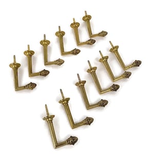 Könnte beinhalten: Zehn goldfarbene Metallhaken mit einem dekorativen Eichel-Design. Die Haken sind L-förmig und haben eine Schraube auf der Rückseite zum Befestigen.