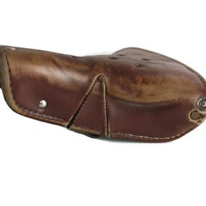May include: A brown leather bicycle saddle with a worn, distressed look. The saddle has a curved shape and is secured with metal rivets.
