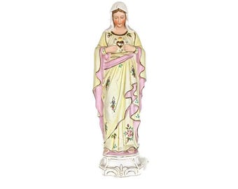 May include: A ceramic statue of a woman in a flowing yellow gown with pink accents. The statue has a white veil and a heart-shaped emblem on the chest. The base is white with decorative scrollwork.