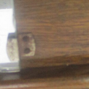 May include: Close-up of a wooden furniture joint with a metal hinge. The wood grain is visible, and the hinge has two holes. The image is well-lit, highlighting the details of the construction.