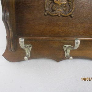 May include: A vintage wooden coat rack with three metal hooks. The rack has a dark brown finish and a decorative carved design at the top. A small mirror is attached on the right side.