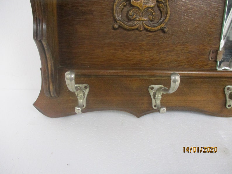 May include: A vintage wooden coat rack with three metal hooks. The rack has a dark brown finish and a decorative carved design at the top. A small mirror is attached on the right side.