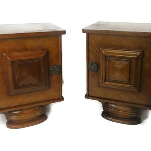 May include: Two wooden nightstands with a single drawer and a cabinet door. Each nightstand has a carved base and a decorative detail on the side.