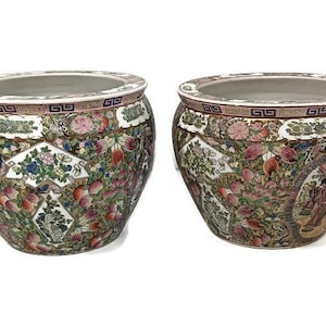 Könnte beinhalten: Zwei große, runde, weiße Keramik-Blumentöpfe mit aufwendigen floralen und geometrischen Mustern in Rosa-, Grün-, Blau- und Goldtönen. Die Töpfe haben eine breite, runde Öffnung und einen leicht abgerundeten Boden.