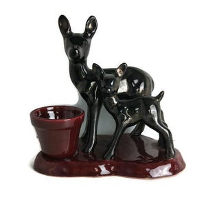May include: A ceramic figurine of a mother deer and her fawn. The deer are black with a glossy finish and stand on a burgundy base. The base has a small planter in the center.