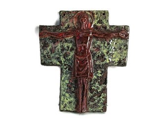 May include: A ceramic wall sculpture of a crucifix with a red figure of Jesus Christ on a green and brown background.