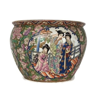 Puede incluir: Una maceta redonda de cerámica con un diseño floral y figurativo detallado. La maceta presenta una escena de mujeres con vestimenta tradicional, rodeadas de flores en tonos rosa, morado y verde. El borde tiene un ribete marrón y dorado.