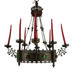 Könnte beinhalten: Ein antiker Kronleuchter mit kronenförmiger Spitze und kreisförmiger Basis. Er verfügt über mehrere rote Kerzen und dekorative Metallarbeiten. Die Basis ist mit farbigen Juwelen verziert, und die Leuchte hängt an Ketten.