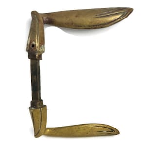 Könnte beinhalten: Ein antiker Türgriff aus Messing mit einem einzigartigen, geschwungenen Design. Der Griff ist aus massivem Messing gefertigt und hat eine glatte, polierte Oberfläche.