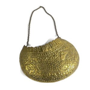 May include: A gold-colored metal hanging basket with an ornate design featuring a floral pattern and a stylized animal. The basket has a chain handle.