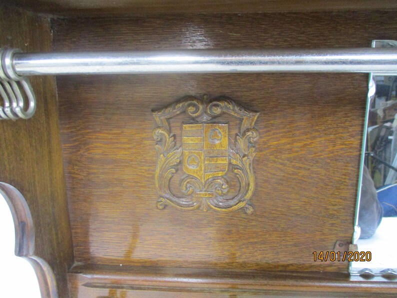 May include: A wooden cabinet with a carved crest and a metal bar. The cabinet is made of dark wood and has a mirror on the right side. The crest is in the center and has a shield design.