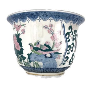 Peut inclure: Un pot en céramique blanche avec un motif floral bleu et vert représentant deux oiseaux. Le pot a un bord festonné et une bordure bleue et blanche.