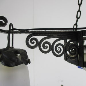 May include: Ornate black metal chandelier with a frosted glass shade. The fixture features decorative scrollwork and leaf accents. The chandelier is suspended by a chain and is designed for indoor lighting.