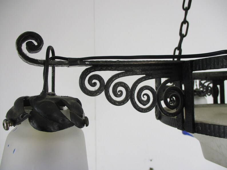 May include: Ornate black metal chandelier with a frosted glass shade. The fixture features decorative scrollwork and leaf accents. The chandelier is suspended by a chain and is designed for indoor lighting.