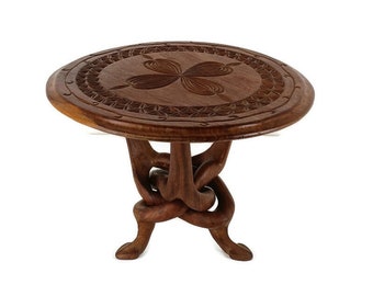May include: A round wooden table with a carved design on the top and a unique knotted base. The table is made of dark brown wood and has a rustic look.