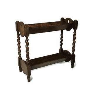 Pode incluir: Uma prateleira de madeira castanha escura de dois níveis com um design vintage. A prateleira apresenta fusos torneados e recortes decorativos. As prateleiras são retangulares e as pernas ligeiramente curvas.