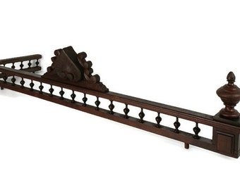 May include: A dark brown wooden fireplace mantel with intricate carvings and finials. The mantel has a decorative design with a central crest and a series of small, round finials along the edges.