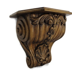 May include: A dark brown wooden shelf bracket with intricate carvings and a scrolled design. The bracket has a scalloped edge and a decorative floral motif.