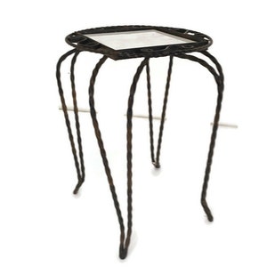 Puede incluir: Una mesa auxiliar de metal negro con tapa redonda y seis patas. La tapa de la mesa tiene un diseño decorativo y una superficie blanca.