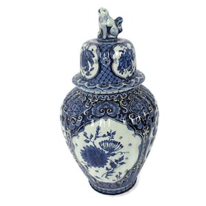 Puede incluir: Un jarrón grande de cerámica azul y blanco con tapa. El jarrón está decorado con motivos florales y geométricos. La tapa tiene una pequeña figura de animal en la parte superior.