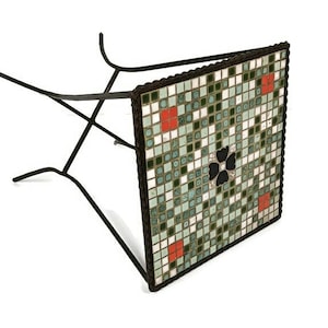 May include: A black metal folding table with a square mosaic tile top. The tiles are green, white, and red with a black clover design in the center.
