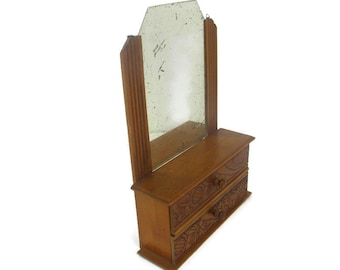 May include: A small wooden vanity with two drawers and a beveled mirror. The drawers have carved floral designs.
