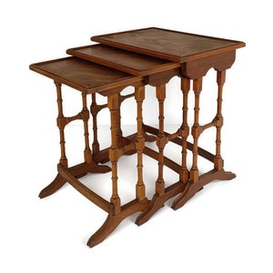 May include: A set of three wooden nesting tables with intricate carved details. The tables are made of dark wood and have a rectangular shape. The top table is slightly larger than the bottom two tables.