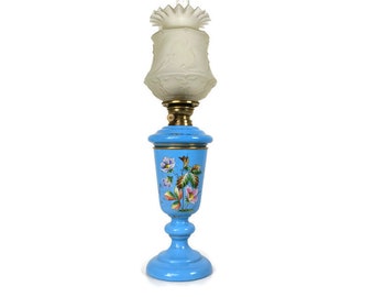 May include: A blue glass oil lamp with a floral design and a white frosted glass shade.